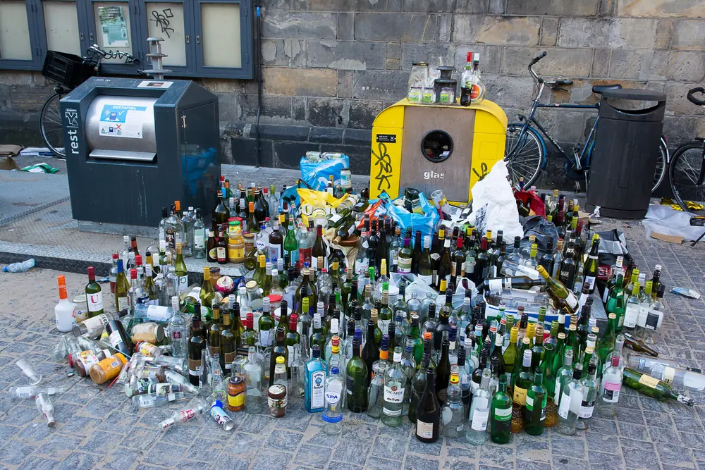 Dutzende leere Flaschen stehen neben überfüllten Glascontainern
